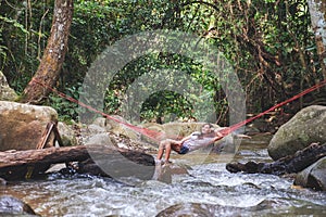 A beautiful young woman sitting and relaxing in hammock in waterfall stream