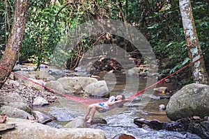 A beautiful young woman sitting and relaxing in hammock in waterfall stream