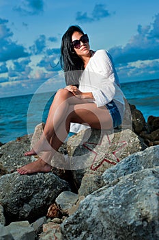 Beautiful young woman sitting on a rock by the ocean