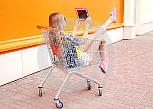 Beautiful young woman sitting in shopping trolley cart over colorful orange
