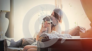 Beautiful young woman sitting on the sofa and hugging her dog in