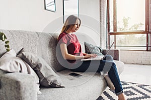 Beautiful young woman sitting on sofa and using laptop at home