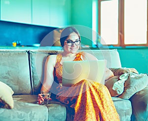 Beautiful young woman sitting on a sofa and working on a laptop