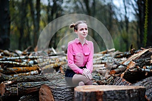 Beautiful young woman sitting on stack of felled tree trunks in the forest