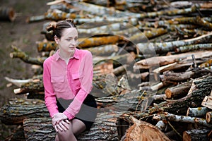 Beautiful young woman sitting on stack of felled tree trunks in the forest