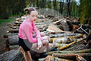 Beautiful young woman sitting on stack of felled tree trunks in the forest