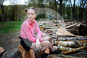 Beautiful young woman sitting on stack of felled tree trunks in the forest