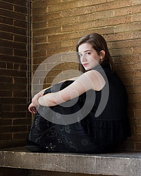 Beautiful young woman sitting on stone bench against brick wall
