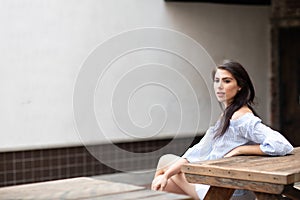 A beautiful young woman sitting at the table at a city park, looking into the distance