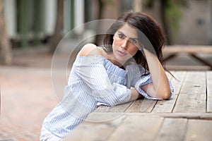 A beautiful young woman sitting at the table at a city park, looking into the distance