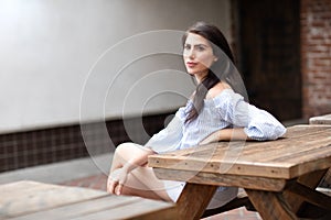 A beautiful young woman sitting at the table at a city park, looking into the distance