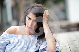 A beautiful young woman sitting at the table at a city park, looking into the distance