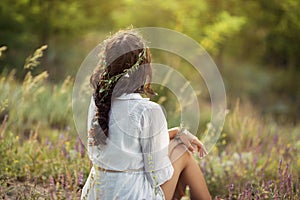 Beautiful young woman sitting in a wheat field in the summer sunset. Beauty and summer concept