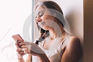 Beautiful young woman sitting on the windowsill listen to music