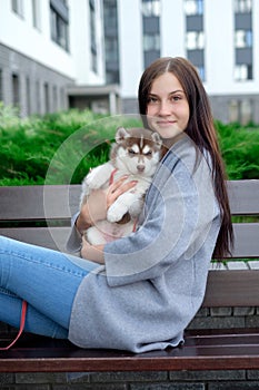 Beautiful young woman sitting on wooden bench and enjoy with her cute little husky puppy