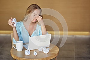 Beautiful young woman sitting on workplace with the laptop and tired crumpling the sheet