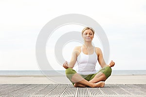 Beautiful young woman sitting in yoga pose at the beach