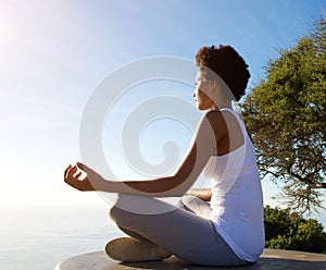 Beautiful young woman sitting in yoga pose at beach