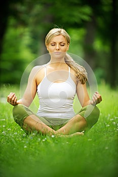 Beautiful young woman sitting in yoga pose in the park