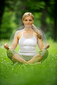 Beautiful young woman sitting in yoga position in the park