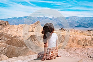 A beautiful young woman in a skirt stands in the middle of a desert landscape in Death Valley Zabriskie Point, USA.