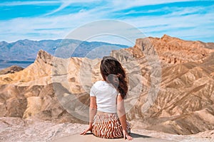 A beautiful young woman in a skirt stands in the middle of a desert landscape in Death Valley Zabriskie Point, USA.