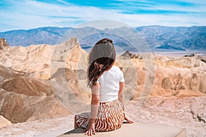 A beautiful young woman in a skirt stands in the middle of a desert landscape in Death Valley Zabriskie Point, USA.