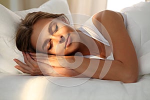 Beautiful young woman sleeping while lying in bed comfortably and blissfully. Sunbeam dawn on her face