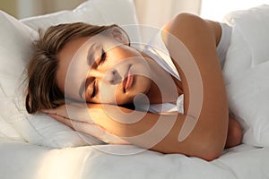 Beautiful young woman sleeping while lying in bed comfortably and blissfully. Sunbeam dawn on her face