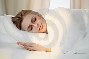 Beautiful young woman sleeping while lying in bed comfortably and blissfully Sunbeam dawn on her face