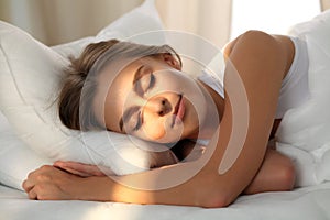 Beautiful young woman sleeping while lying in bed comfortably and blissfully. Sunbeam dawn on her face