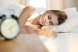 Beautiful young woman sleeping while lying in bed comfortably and blissfully Sunbeam dawn on her face