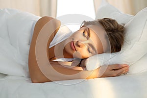 Beautiful young woman sleeping while lying in bed comfortably and blissfully Sunbeam dawn on her face