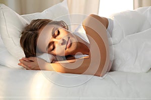 Beautiful young woman sleeping while lying in bed comfortably and blissfully. Sunbeam dawn on her face