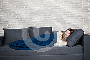 Beautiful young woman is sleeping and seeing sweet dreams on sofa at home