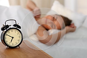 Beautiful young woman sleeping and smiling while lying in bed comfortably and blissfully on the background of alarm