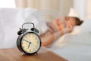 Beautiful young woman sleeping and smiling while lying in bed comfortably and blissfully on the background of alarm