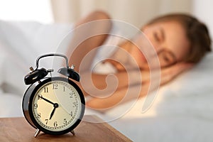 Beautiful young woman sleeping and smiling while lying in bed comfortably and blissfully on the background of alarm