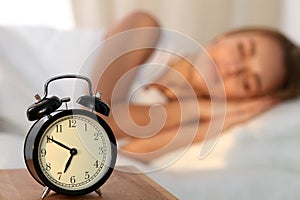 Beautiful young woman sleeping and smiling while lying in bed comfortably and blissfully on the background of alarm