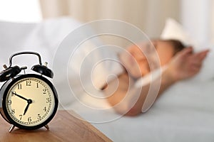 Beautiful young woman sleeping and smiling while lying in bed comfortably and blissfully on the background of alarm