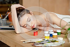 beautiful young woman sleeping on table with paints