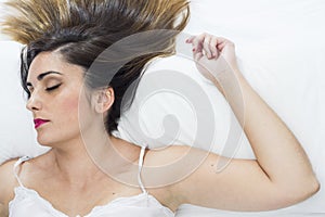 Beautiful young woman sleeping very relaxed on a white bed with a white nightgown