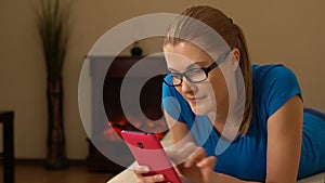 Beautiful young woman with a smartphone lying on a sofa. Browsing Internet and smiling. 00355