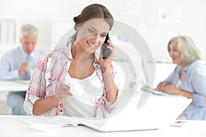 Beautiful young woman with smartphone working in office, colleagues on bckground