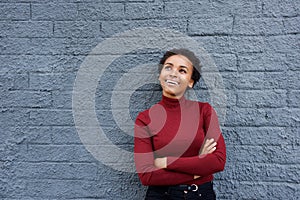 Beautiful young woman smiling against gray wall with arms crossed