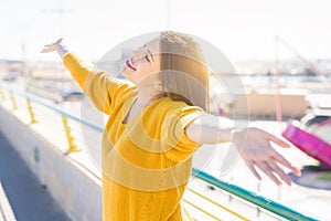 Beautiful young woman smiling with closed eyes and open arms enjoying the sunlight on a sunny day. Happy sunbathe