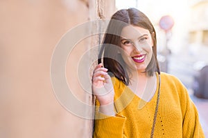 Beautiful young woman smiling confident and cheerful leaning on bricks wall, walking on the street of the city on a sunny day