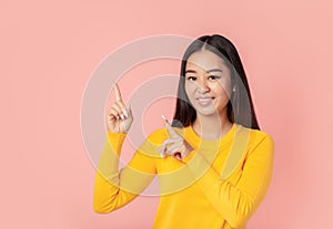 Beautiful young woman smiling with his finger pointing on pink background with copy space, smiles friendly