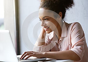 Beautiful young woman smiling and looking at laptop screen photo