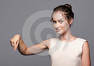 Beautiful young woman smiling and pointing down at copy space on gray background